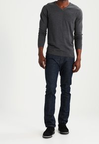 Grå v-ringad tröja i stickat tyg, matchad med mörkblå slim fit-jeans och svarta sneakers med vita sulor.