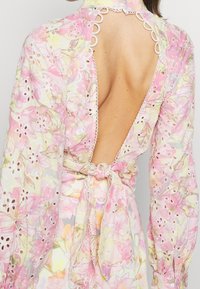 Robe à imprimé floral en tissu léger, manches longues, dos ouvert, bordure en dentelle festonnée et taille nouée, dans des couleurs pastel.