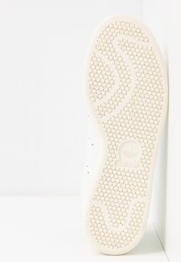 Adidas vit sneaker-sula med cirkulär texturerad grepp och logotyp präglad i centrum, placerad vertikalt mot en vit bakgrund.