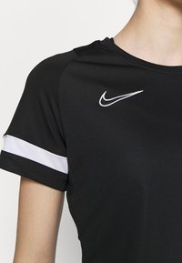 Svart idrottströja med korta ärmar, med en vit Nike-logotyp på bröstet och vit kantning med nättextur på ärmsluten.