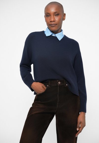 Mornarska pulover od mekog pletenog materijala, s klasičnim okruglim izrezom. Uparen s smeškim hlačama visokog struka i svijetloplavom košuljom s kragnom.