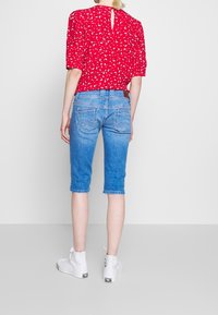 Top rojo de manga corta con estampado floral blanco, combinado con jeans azul claro hasta la rodilla. Zapatillas blancas de caña alta completan el look.