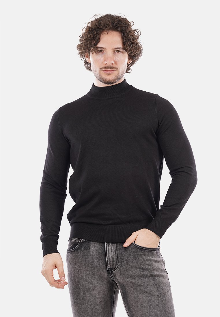 Maglione a collo alto nero realizzato in un tessuto a coste. Design aderente con maniche lunghe e una texture liscia, abbinato a jeans scuri.