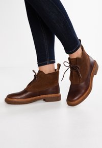 Botas de tobillo con cordones marrones que presentan una combinación de cuero liso y ante, una puntera redondeada y una suela de goma ligera.
