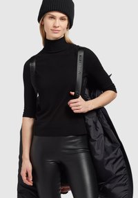 Sort turtleneck med tætsiddende ærmer, parret med sorte bukser i faux læder. En sort dunjakke hænger over den ene skulder.