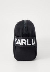Juodas nailoninis kosmetikos krepšys su tekstūruota danga, viršutinė užtrauktuko uždarymo sistema ir ryški baltą "KARL" logotipas ant nertos juostos.