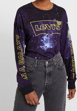 Person wearing a cosmic-themed black Levi's long-sleeve shirt with yellow text, paired with high-waisted dark gray jeans.