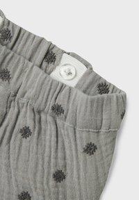 Tissu en coton gris avec une surface texturée et froissée, comportant des pois noirs éparpillés et une fermeture à bouton blanche à la taille.