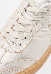 Lyse sølvfarvede sneakers med tekstureret syntetisk overdel, beige snørebånd og sål af gummigummi. Syning detaljer fremhæver designet.