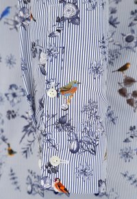 Koszula w paski z haftem w kwiaty i ptaki; kolory niebieski i biały; teksturowany materiał; posiada zapięcie na guzik przy mankiecie.