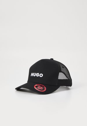 Μαύρο καπέλο trucker φτιαγμένο από ύφασμα με πλέγμα στα πλάγια, με λευκό κεντημένο λογότυπο "HUGO" στο μπροστινό μέρος και κυκλική κόκκινη ετικέτα στο γείσο.