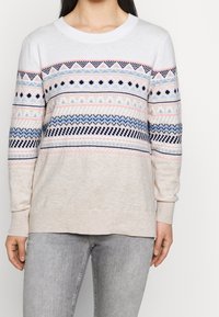 Jersey de color beige claro con un cuello redondo, que presenta un vibrante patrón de triángulos y formas geométricas en azul marino, rosa y azul claro.