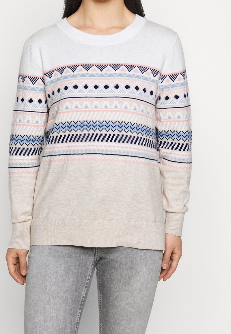 Jersey de color beige claro con un cuello redondo, que presenta un vibrante patrón de triángulos y formas geométricas en azul marino, rosa y azul claro.