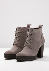 Gray suede ankle boots with a stacked heel, lace-up design, and subtle branding on the side. Flat rubber sole for grip.