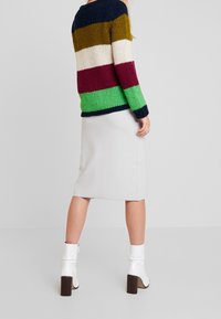 Suéter de punto con rayas en azul marino, verde, burdeos, blanco y olivo; combinado con una falda gris y botas blancas con tacones cuadrados.
