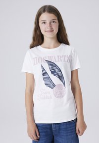 Witte katoenen t-shirt met de tekst "Hogwarts" in het roze, en een Quidditch-thema grafiek: een gevleugelde bal met gedetailleerde strepen en accenten.