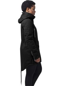 Veste noire à manches longues avec capuche, dotée d'une fermeture éclair à l'avant, de poches latérales et d'un ourlet à cordon. Tissu texturé avec une silhouette ajustée.