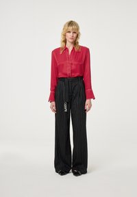 Rode doorzichtige blouse met knoopsluiting, lange mouwen; zwarte pinstriped wijde broek met versieringen, gedragen met zwarte schoenen.
