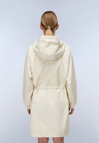 Giacca da pioggia beige chiaro con cappuccio, vita stretta, polsini elasticizzati e una texture leggermente lucida, che arriva fino a metà coscia sul retro.