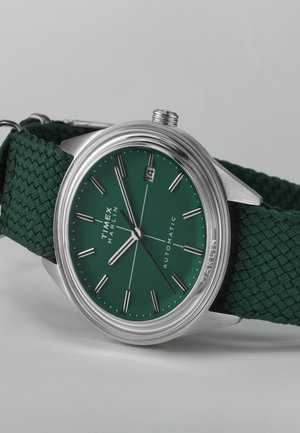 Ročna ura Timex Marlin z ohišjem iz nerjavečega jekla, zelenim teksturiranim številčnico, srebrnimi oznakami ur in zelenim pletenim tekstilnim pasom. Vključeno okno za datum.