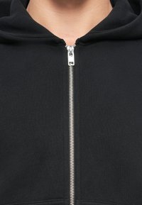 Czarna bluza z kapturem na zamek, wykonana z miękkiego materiału o teksturowanym wykończeniu. Posiada srebrny metalowy zamek oraz kaptur. Prosty design, bez wzorów.
