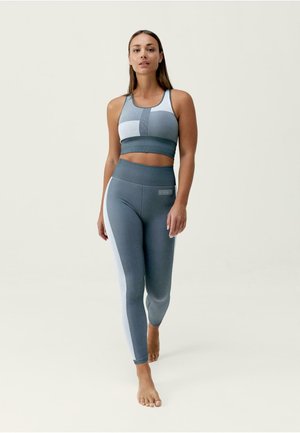 Grijze sportoutfit bestaande uit een cropped sportbh en high-waisted leggings met contrasterende lichtgrijze paneelaccenten. Gladde, rekbare stof.