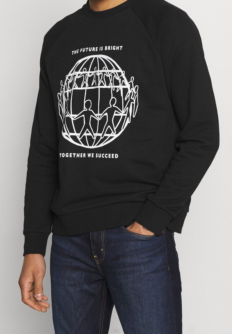 Sweat-shirt noir avec un graphisme blanc de bonshommes en bâton tenant la main autour d'un globe et texte indiquant "The future is bright together we succeed."