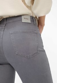 Graue Jeans aus Denim verfügen über eine abgerundete Gesäßtasche mit dekorativer Stickerei, ein sichtbares Logo-Patch am Bund und ein glattes, tailliertes Design.