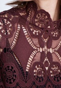 Bordeaux blond med blomster mønstre og udsugningsdetaljer, lagdelt over en sort bund. Har indviklet broderi og teksturvariationer.