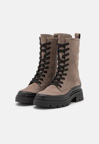 Lace-up enkelboots in taupe suède, met een dikke zwarte rubberen zool en teenkap, voorzien van zwarte veters en een lus aan de achterkant.