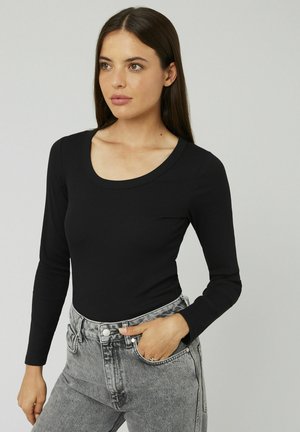 Haut noir à manches longues avec un décolleté en forme de cœur, fabriqué en matière côtelée, associé à un jean gris taille haute avec des poches avant.