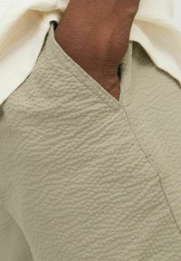 Gai pelēks audums ar viegli sakostu izskatu, ar V veida kakla izgriezumu. Virsū ir redzama krēma krāsas kārta.