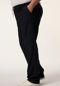Pantaloni blu scuro con vestibilità comoda, vita con cordoncino, tasche laterali e texture liscia. Abbinati a sneakers bianche.