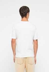 Hvit bomull t-skjorte med korte ermer, rund halsutskjæring, avslappet passform, sett fra baksiden, kombinert med lyse denim bukser.
