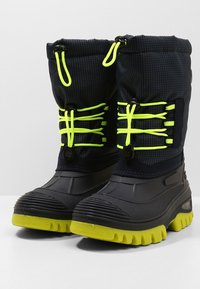 Bottes imperméables noires à surface texturée, lacets jaune néon et semelles en caoutchouc avec des rainures profondes pour une meilleure traction. Manchette ajustable en haut.