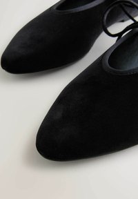 Pantofole din suede negru cu vârful ascuțit și textură netedă. Prezintă un rim subtil din satin în jurul deschiderii și o detaliu minimalist cu șnur.