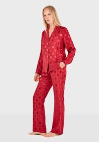 Pijamas de satén rojo que presentan una blusa con botones, un bolsillo y mangas largas, combinados con pantalones a juego adornados con grandes lunares.