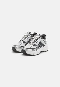 Klobige Sneakers mit einem Obermaterial aus Mesh und Synthetik, überwiegend weiß mit schwarzen Akzenten, strukturierter Sohle und reflektierenden Details an den Schnürsenkeln.