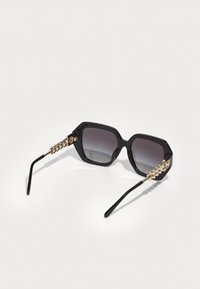 Ochelari de soare negri, supradimensionați, în formă octogonală, cu lentile degradate, având brațe accentedate cu lanțuri aurii și brațe negre elegante.