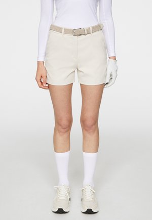 Beige golf shorts with a woven belt, featuring side pockets. Worn with white knee-high socks and light sneakers, offering a casual fit.