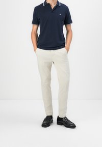 Marineblauwe poloshirt met witte kraagtrim, beige chino's en zwarte loafers. De outfit heeft strakke lijnen en een getailleerde silhouet.
