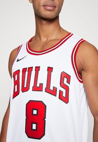 Maglia da basket bianca con testo "Bulls" rosso e nero e numero 8. Il design include un bordo rosso lungo il collo e le maniche, con un logo Nike.