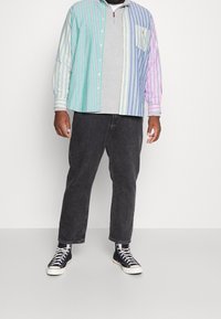 Camisa de botones a rayas en colores pastel, superpuesta sobre una camiseta gris de cuello redondo. Combinada con jeans negros y zapatillas negras.