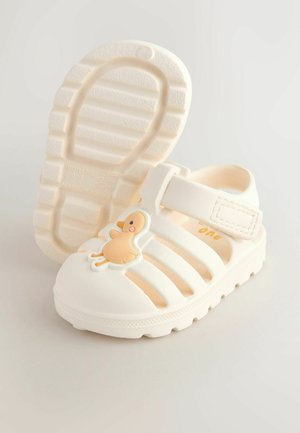 Fehér gumipapucs szellőző kialakítással, elöl kacsafióka hímzéssel és tépőzáras pánttal a biztonságos illeszkedésért. Texturált talp.