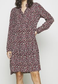 Červené a námořnické květinové šaty s dlouhými rukávy, zapínacím límcem, nařaseným pasem a vícevrstvou sukní. Materiál má měkkou texturu a malé, barevné vzory.