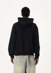 Svart hettegenser med avslappet passform, med kengurulomme og ribbestrikket kant. Kombinert med lyse, baggy jeans.