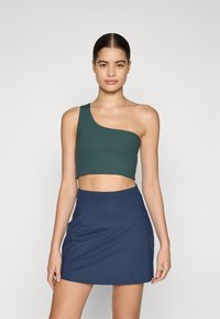 Ühe õlavarrega tume rohelise värviga lühike topp, millele on lisatud tumesinine mini-seelik, valmistatud siledast ja venivast kangast, millel on sobiv siluett.