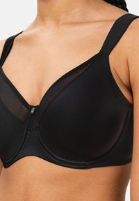 Musta alla oleminen rintaliivi, jossa on sileä kangas, verkko-yksityiskohtia ja säädettävät olkaimet. Ominaisuuksiin kuuluu hienovarainen etulukko ja klassinen kupin muoto.