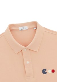 Bleek perzikkleurig polo shirt met een textuurrijke brei, drieknoopsluiting en borduursel van Pac-Man met cirkels in rood en wit.