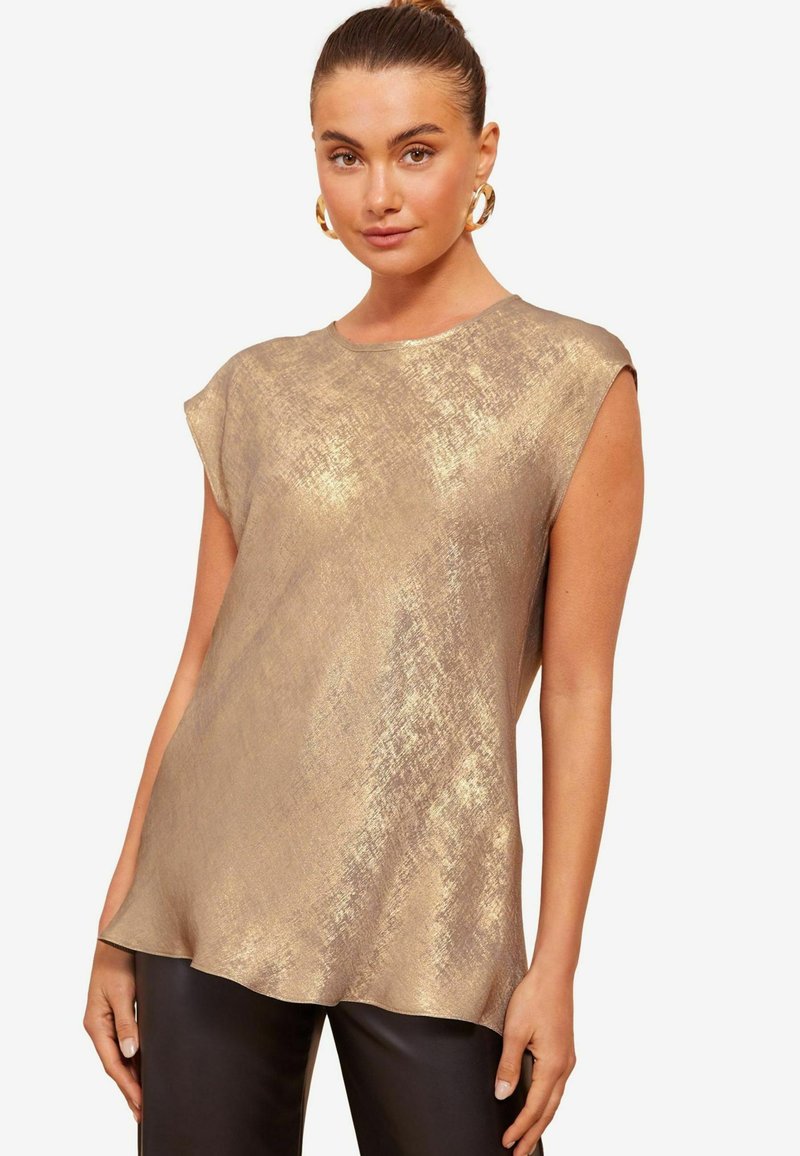Top metallico oro con maniche corte, caratterizzato da una superficie texturizzata e un collo rotondo. Tessuto morbido, orlo leggermente asimmetrico.